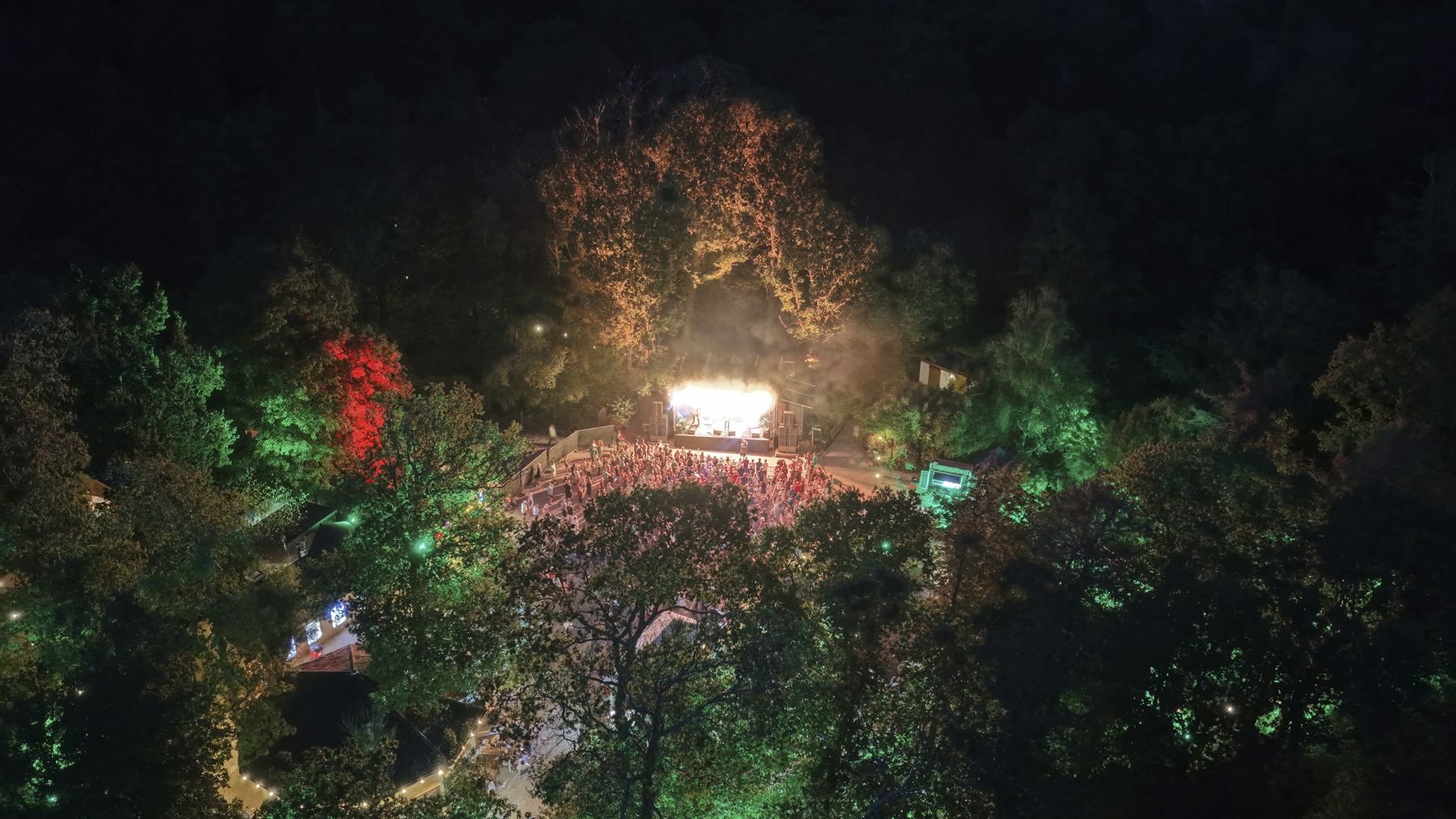 Aerial view of The Woodland Venue at Robin Hill at night, stage lit white with green and red uplit trees